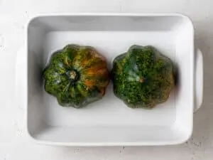 Halved acorn squash flesh-side-down in a ceramic baking dish.