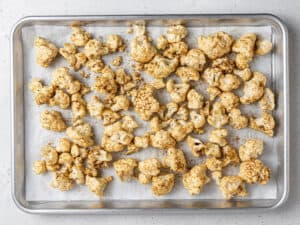 Seasoned cauliflower florets on a lined baking sheet.