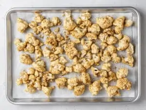 Seasoned cauliflower florets on a lined baking sheet.