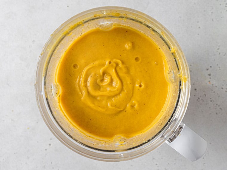 This curried acorn squash soup recipe is cozy and creamy, packed with roasted cauliflower, veggies, and spices. Vegan and freezer-friendly! Overhead view of pureed acorn squash soup in a blender.