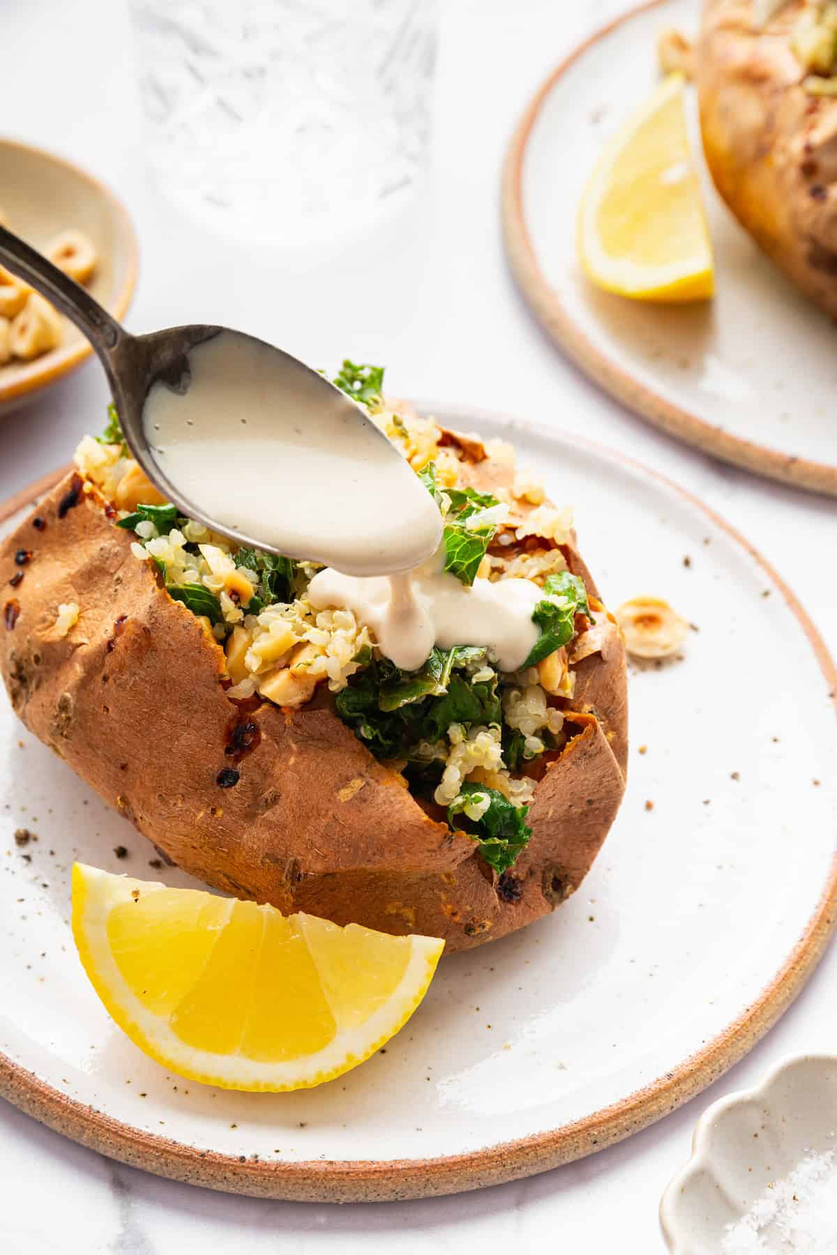 These Stuffed Sweet Potatoes are filled with quinoa, kale and hazelnuts, then topped with creamy tahini sauce. A hearty main or side dish! Spoon drizzling tahini sauce onto stuffed sweet potato.
