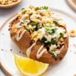 Stuffed sweet potato with kale, quinoa, and tahini sauce on plate.