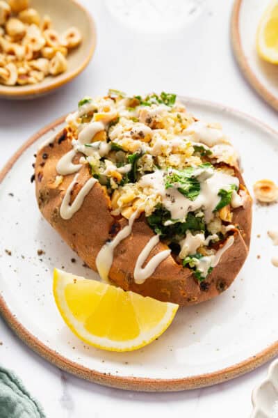 Stuffed sweet potato with kale, quinoa, and tahini sauce on plate.