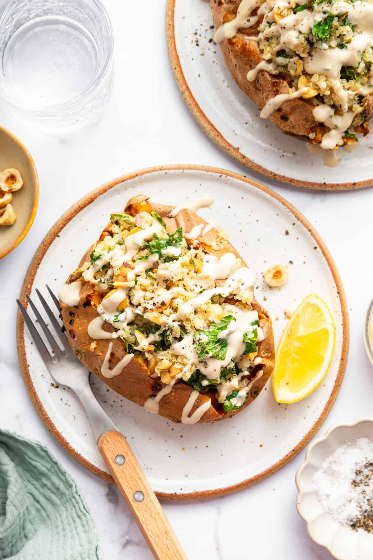 These Stuffed Sweet Potatoes are filled with quinoa, kale and hazelnuts, then topped with creamy tahini sauce. A hearty main or side dish! Two stuffed sweet potatoes with tahini sauce on plates.