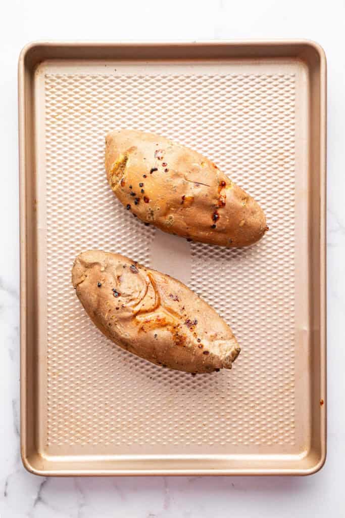 These Stuffed Sweet Potatoes are filled with quinoa, kale and hazelnuts, then topped with creamy tahini sauce. A hearty main or side dish! Two baked sweet potatoes on sheet pan.