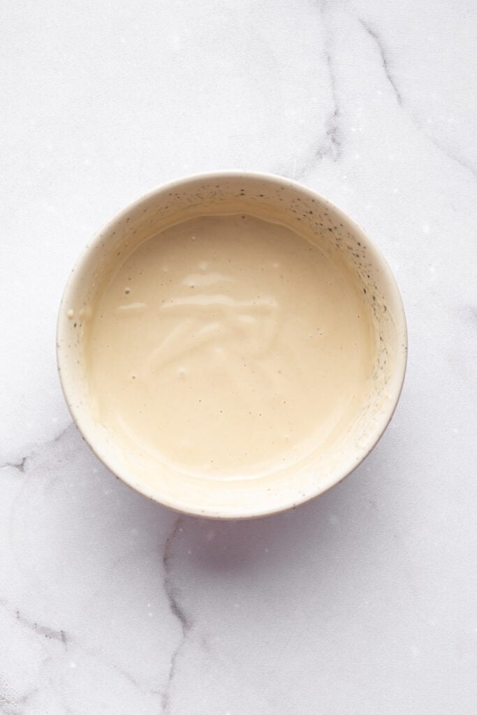 These Stuffed Sweet Potatoes are filled with quinoa, kale and hazelnuts, then topped with creamy tahini sauce. A hearty main or side dish! Tahini sauce in small bowl.