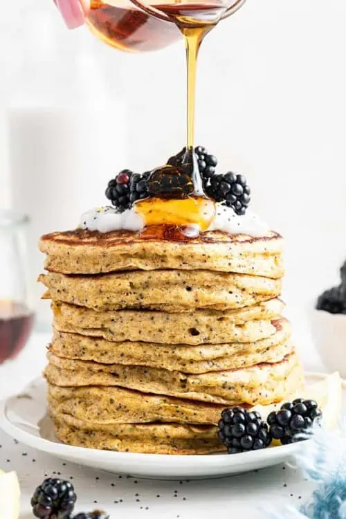 Pouring maple syrup onto stack of lemon poppy seed pancakes