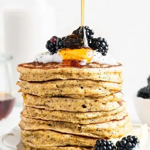 Pouring maple syrup onto stack of lemon poppy seed pancakes