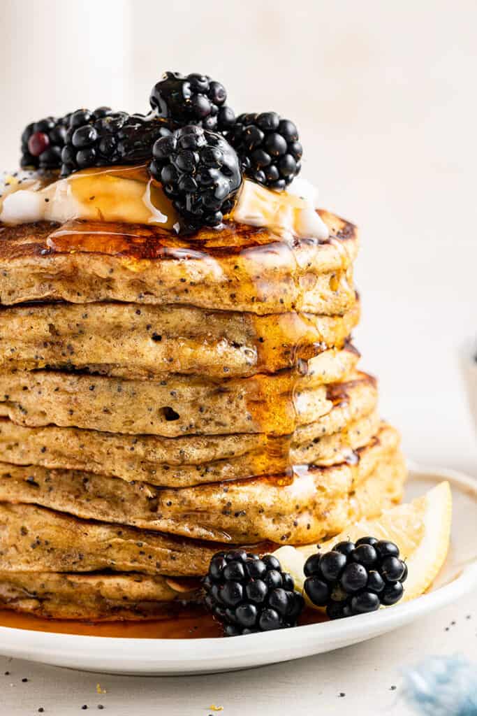 Stack of lemon pancakes with poppy seeds on plate with maple syrup