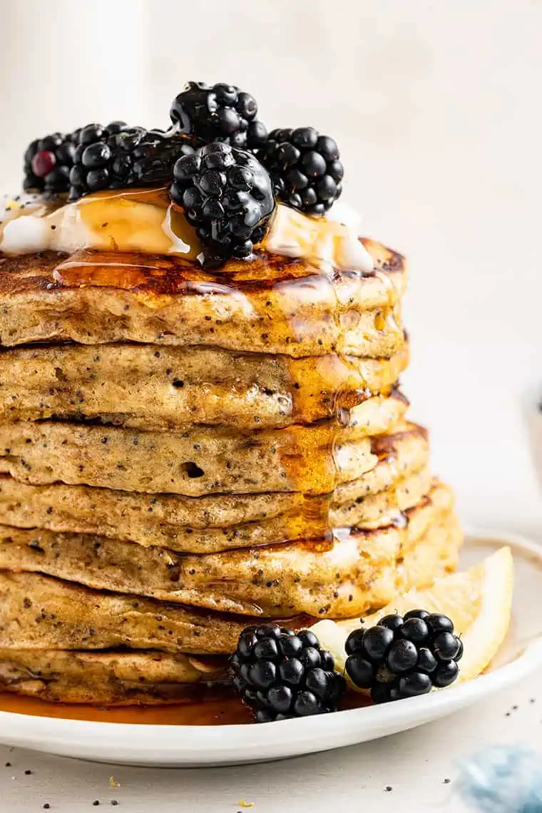 Stack of lemon pancakes with poppy seeds on plate with maple syrup