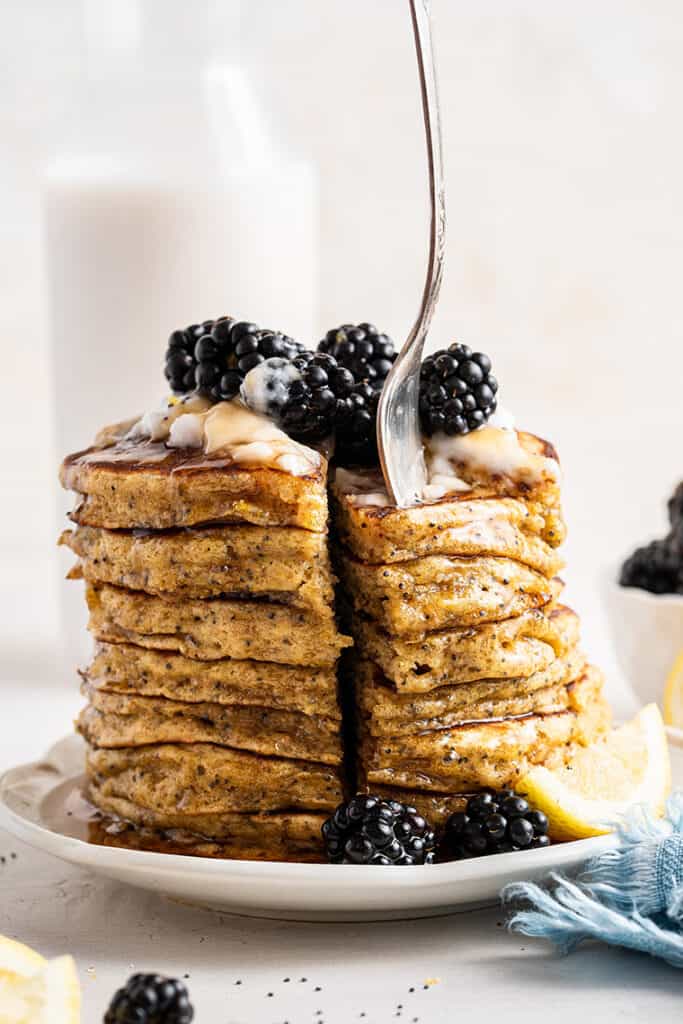 Stack of lemon pancakes topped with yogurt, blackberries, and syrup being cut with a fork