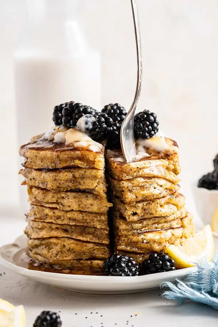 Stack of lemon pancakes topped with yogurt, blackberries, and syrup being cut with a fork