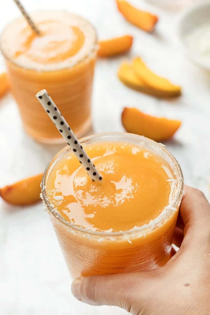 This easy 3-Ingredient Mango Peach Frosé recipe is the ultimate summer cocktail! It's naturally sweet, refreshing, and perfect for a hot day! Hand holding glass of mango peach frose with straw
