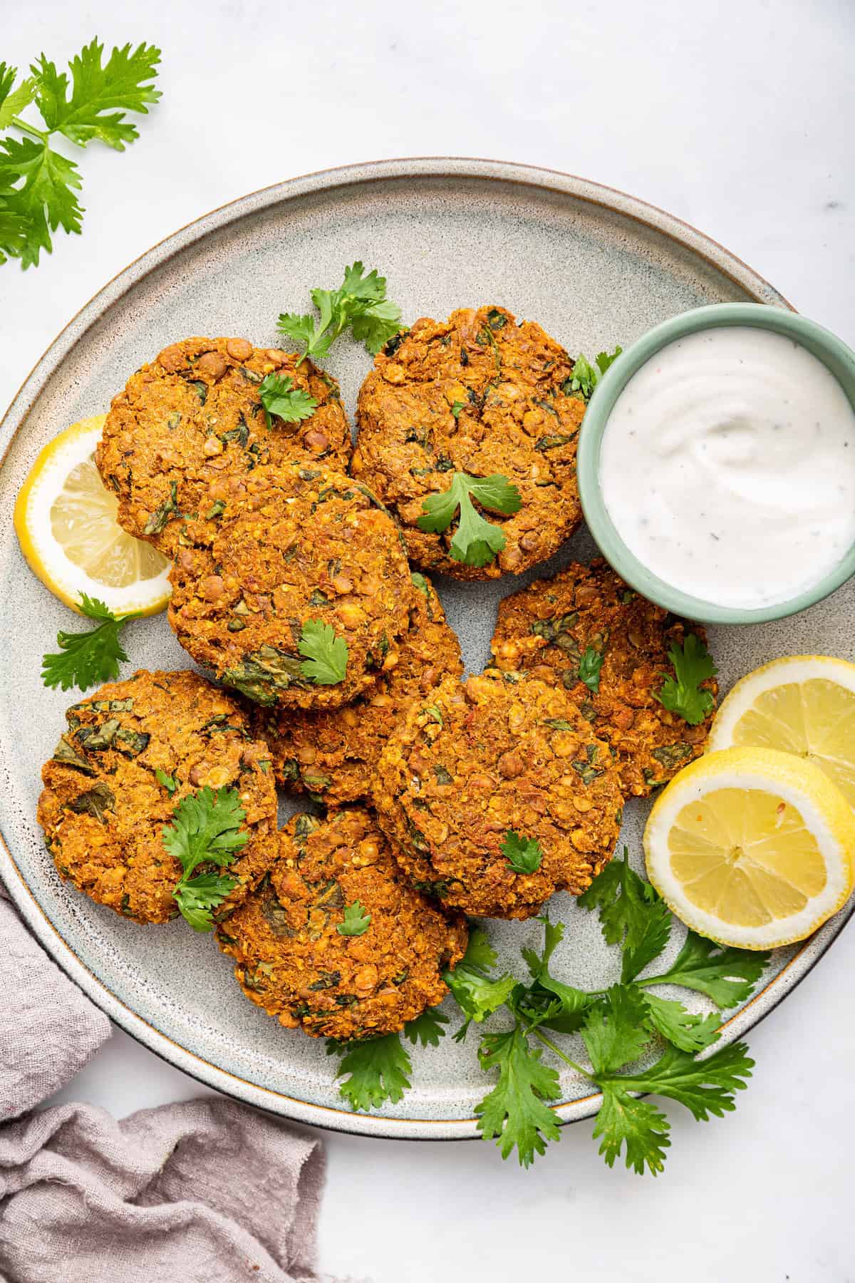 Crispy lentil patties are packed with plant protein and perfect to serve as veggie burgers, appetizers, or as a side. So easy to make too! Overhead view of lentil patties on plate with cup of sauce and lemon slices