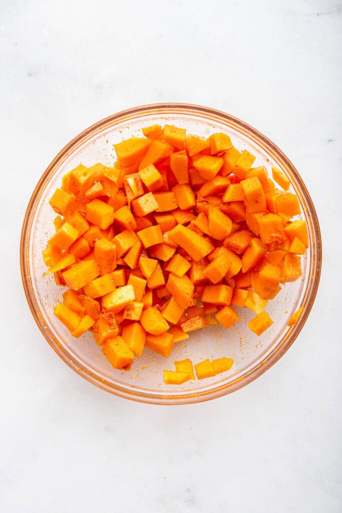Overhead view of seasoned butternut squash in mixing bowl