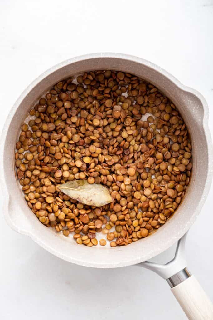 Overhead view of cooked lentils in pan with bay leaf