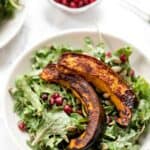 Overhead view of acorn squash salad served on a plate, next to a small bowl of pomegranate seeds.