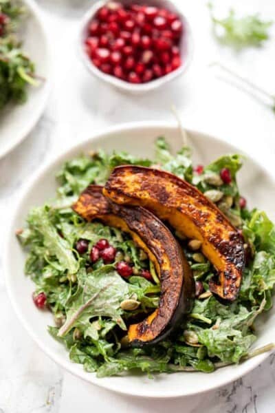 Overhead view of acorn squash salad served on a plate, next to a small bowl of pomegranate seeds.