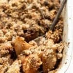 Gluten-free apple crisp in a baking dish with a spoon scooping a serving from the corner.