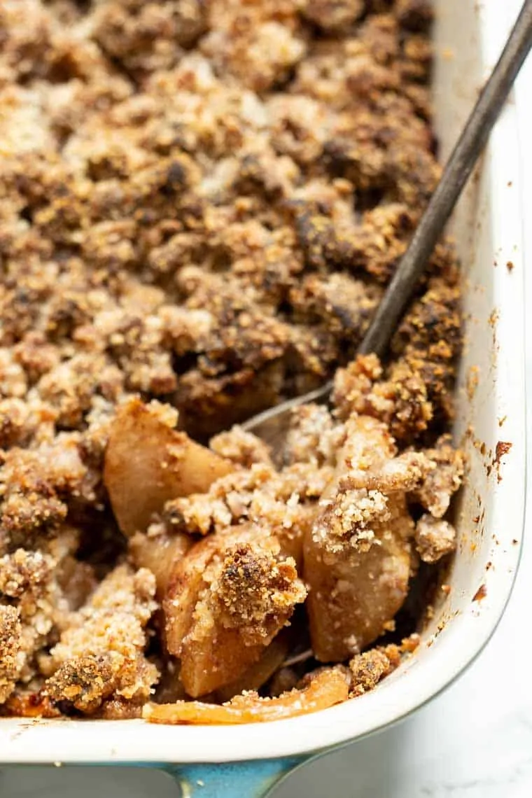 Close up of a gluten-free apple crisp in a baking dish, with a serving spoon in the corner started to disrupt the crisp