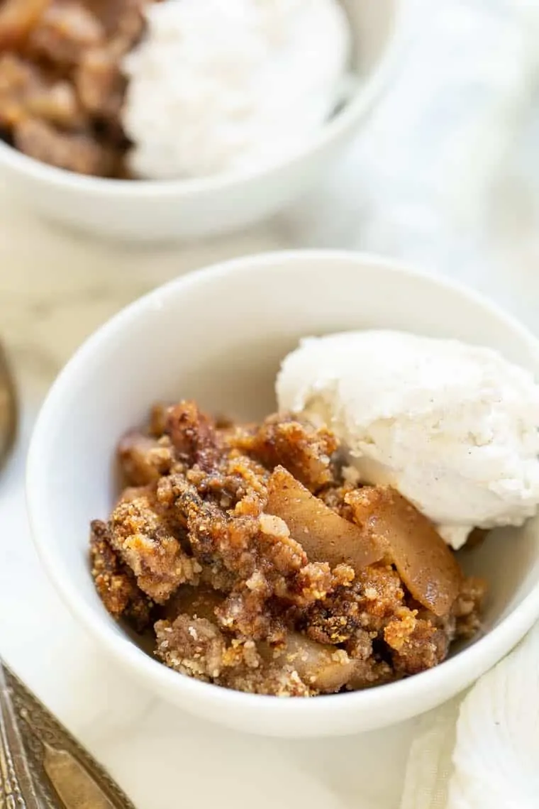 A healthy, vegan, gluten-free apple crisp recipe with fall flavors like cinnamon and maple syrup, and a crunchy topping of dates and pecans A bowl of gluten-free apple crisp with a spoonful of ice cream, with another bowl in the background