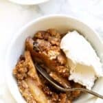 Overhead view of a bowl of gluten-free apple crisp topped with a scoop of vegan ice cream, with a spoon.