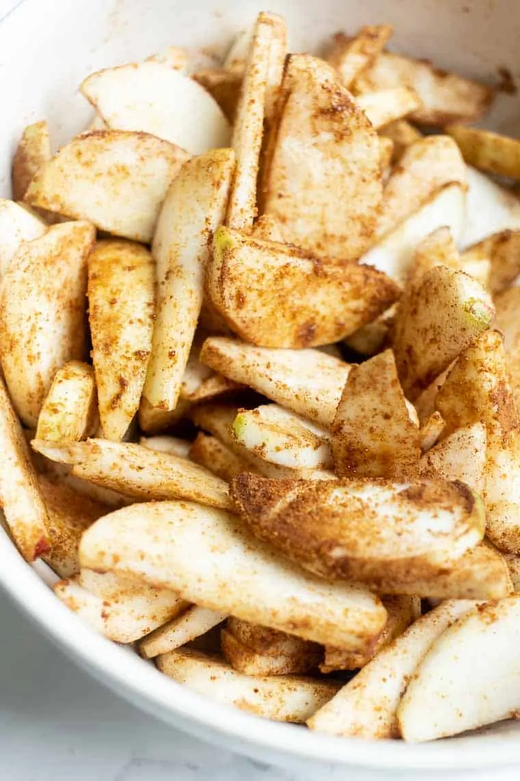 Close up of uncooked apple slices sitting in a bowl, covered in cinnamon and sugar