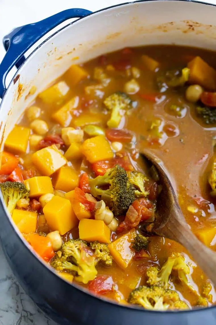 A dutch oven filled with vegetable curry, with a wooden spoon in it