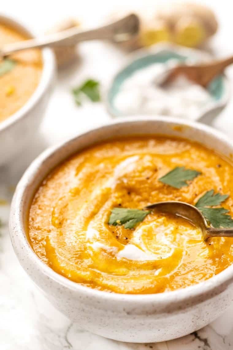 A bowl of turmeric carrot soup, topped with vegan coconut yogurt and parsley, with a spoon in it
