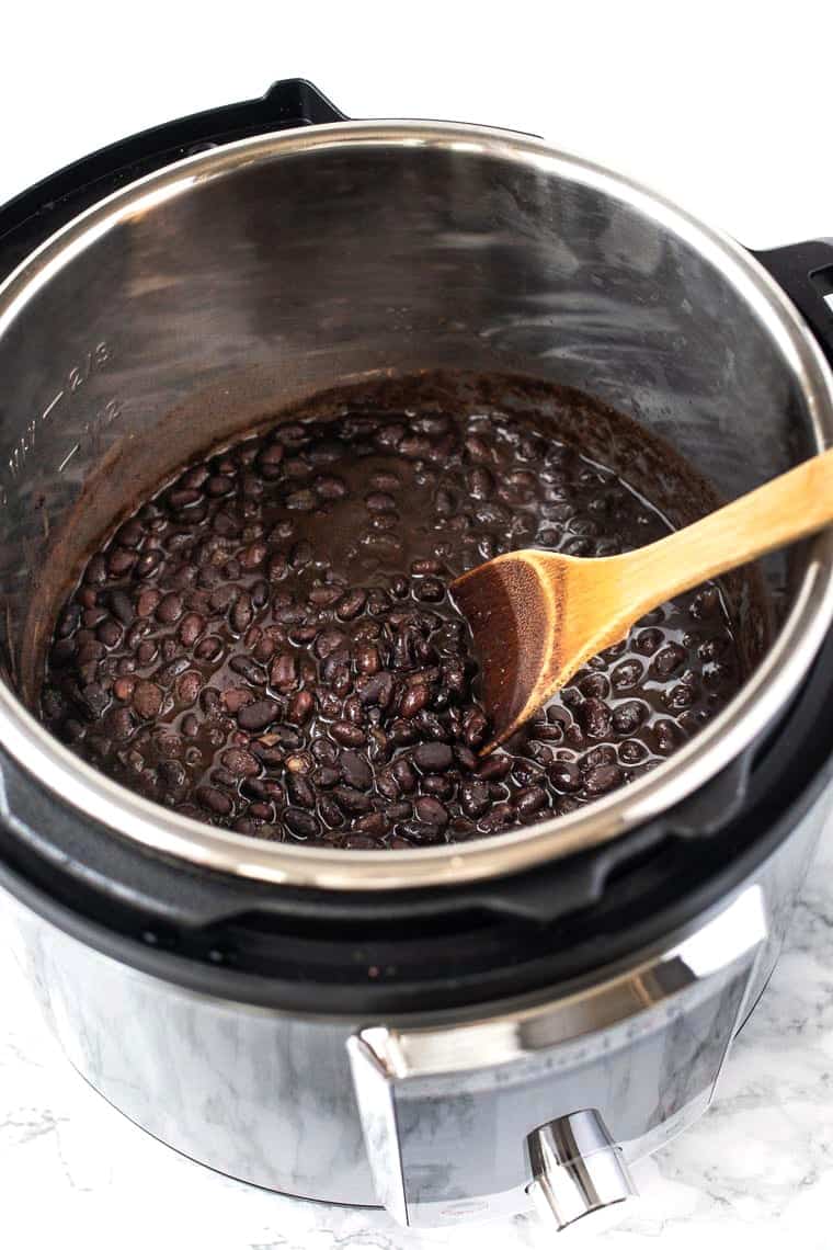 Wooden spoon stirring black beans in Instant Pot