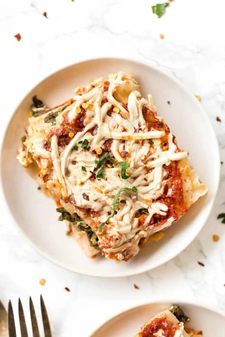 Butternut squash lasagna is made with layers of mashed butternut squash, sauteed spinach, homemade tofu ricotta, and tomato sauce. A slice of vegan butternut squash lasagna on a plate