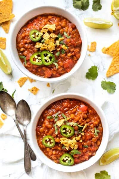 Overhead view of two bowls of lentil chili garnished with tortilla chips, cilantro, and jalapeños