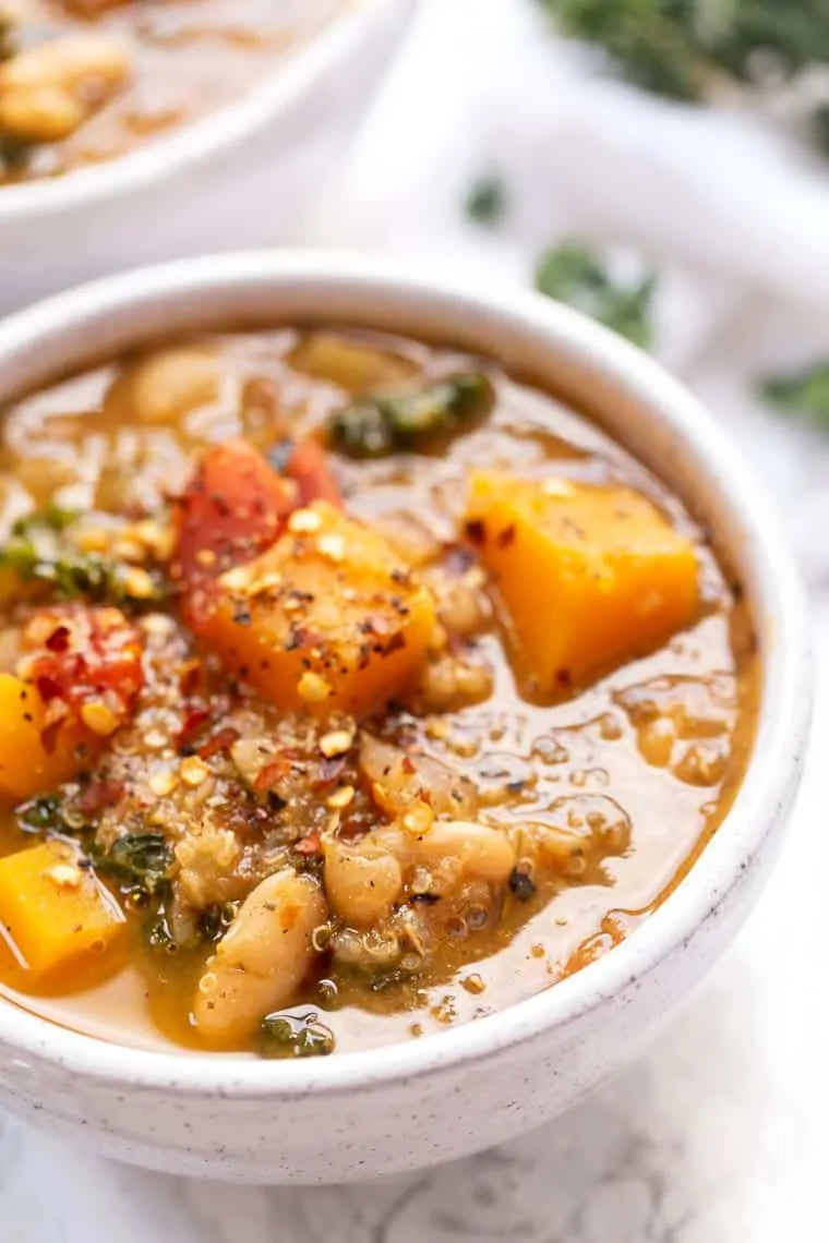 Close up of a bowl of soup with pieces of squash and white beans on top, garnished with chili flakes