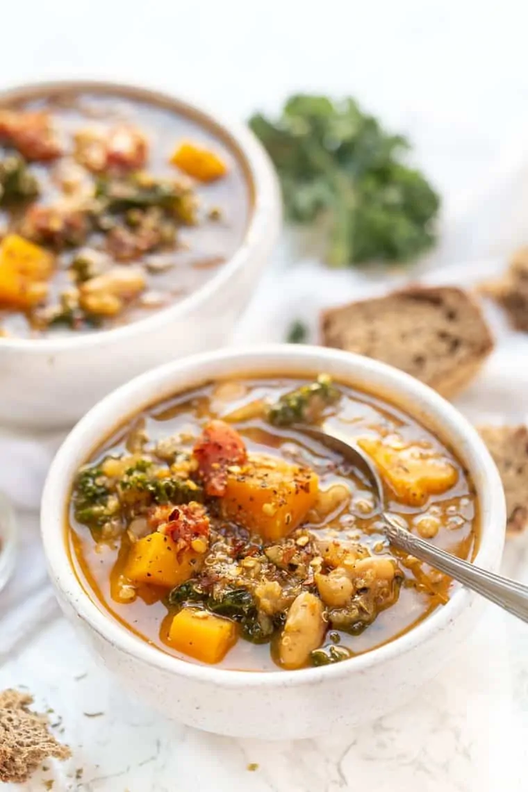 This Tuscan-inspired kale and white bean soup is rich and comforting, filled with flavorful veggies and hearty beans. Perfect for chilly days! A bowl of Tuscan kale white bean soup with a second bowl in the background.