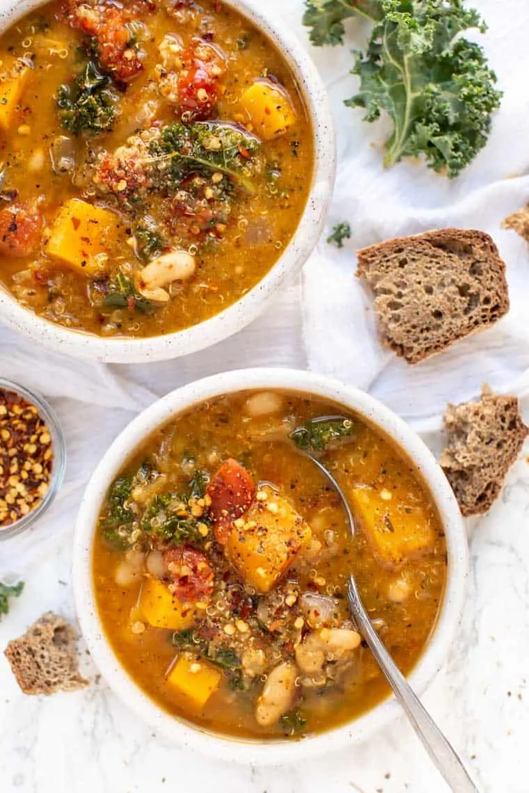 Overhead view of bowls of Tuscan kale white bean soup next to bread pieces.