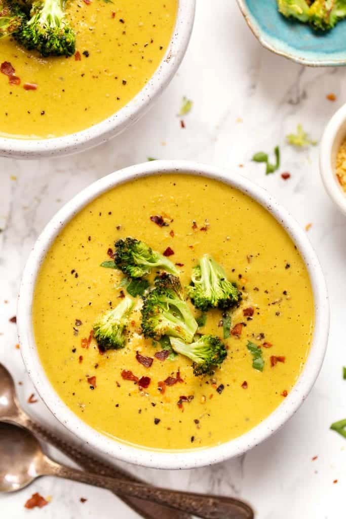 Overhead view of creamy vegan broccoli soup in white bowl garnished with broccoli florets