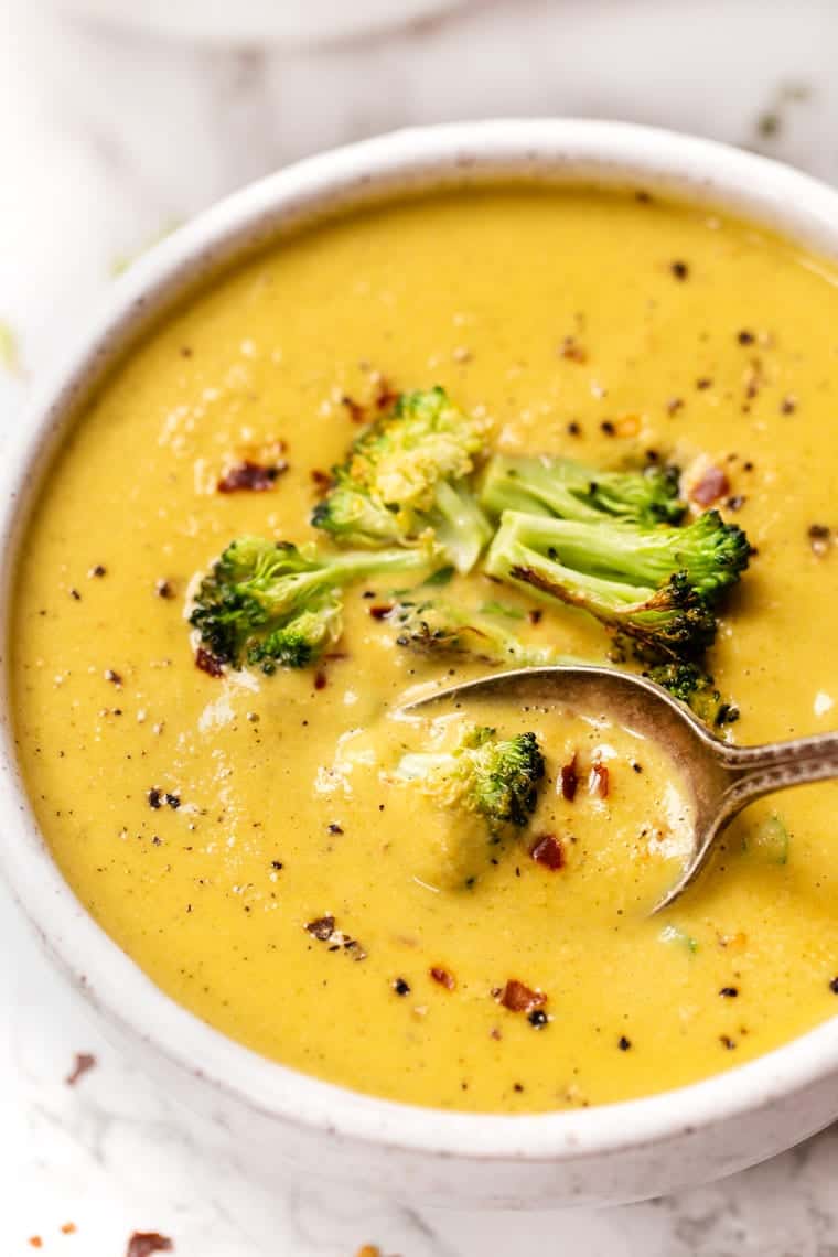 Spoon in bowl of creamy broccoli soup, garnished with broccoli florets and red pepper flakes