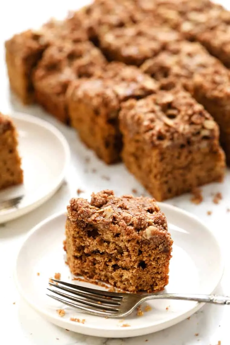 Piece of gluten-free coffee cake on white plate with fork, with remaining cake in background