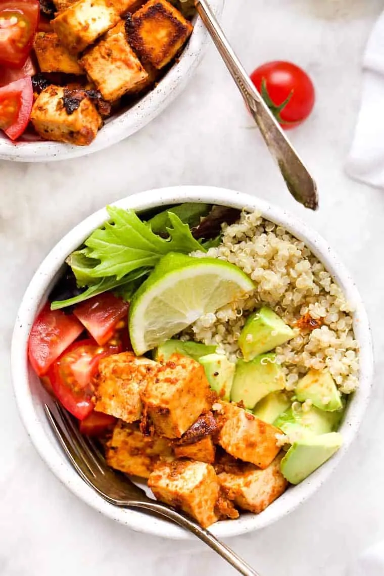 A bowl of quinoa, avocado, tofu, tomatoes, and greens, with a slice of lime and a form