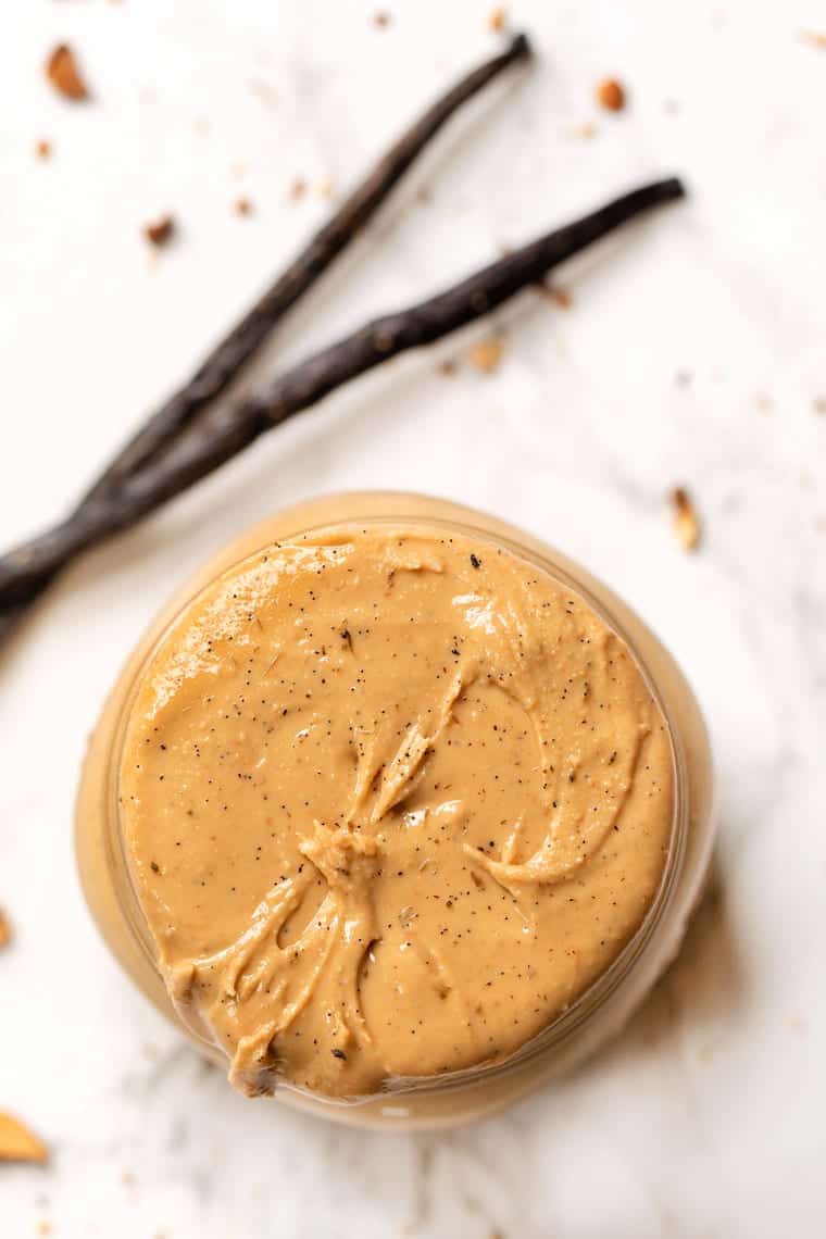 Overhead view of a full jar of vanilla bean cashew butter, with vanilla beans in the background