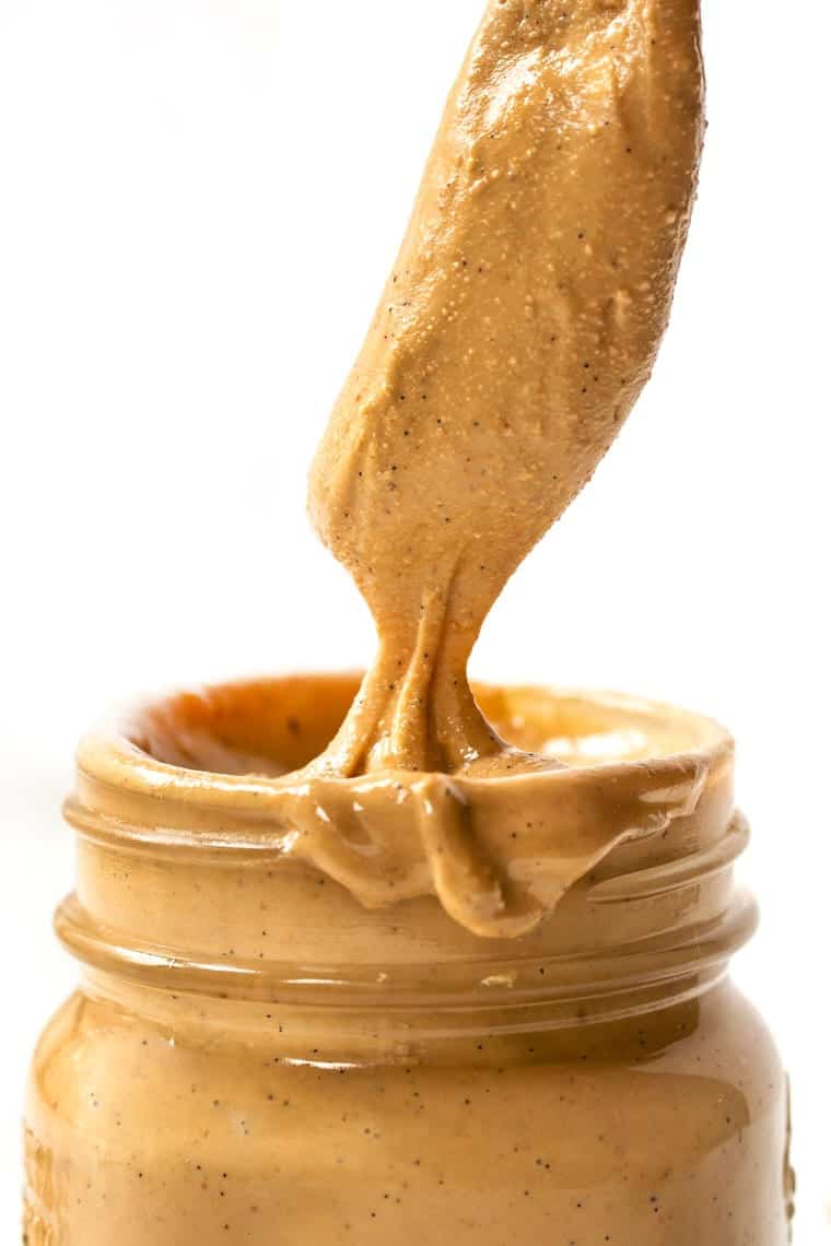 A spoon pulling a spoonful of vanilla bean cashew butter out of a jar