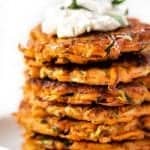 Stack of veggie fritters with cream cheese and herbs on top.