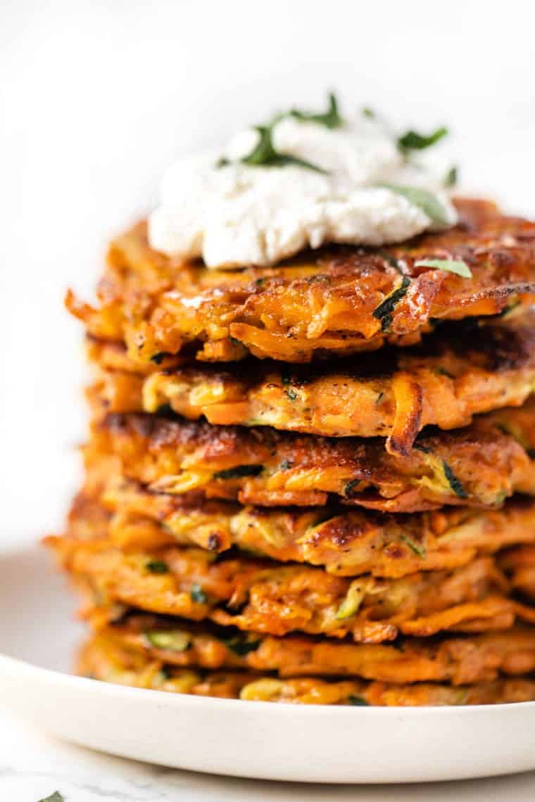 Stack of veggie fritters with cream cheese and herbs on top.