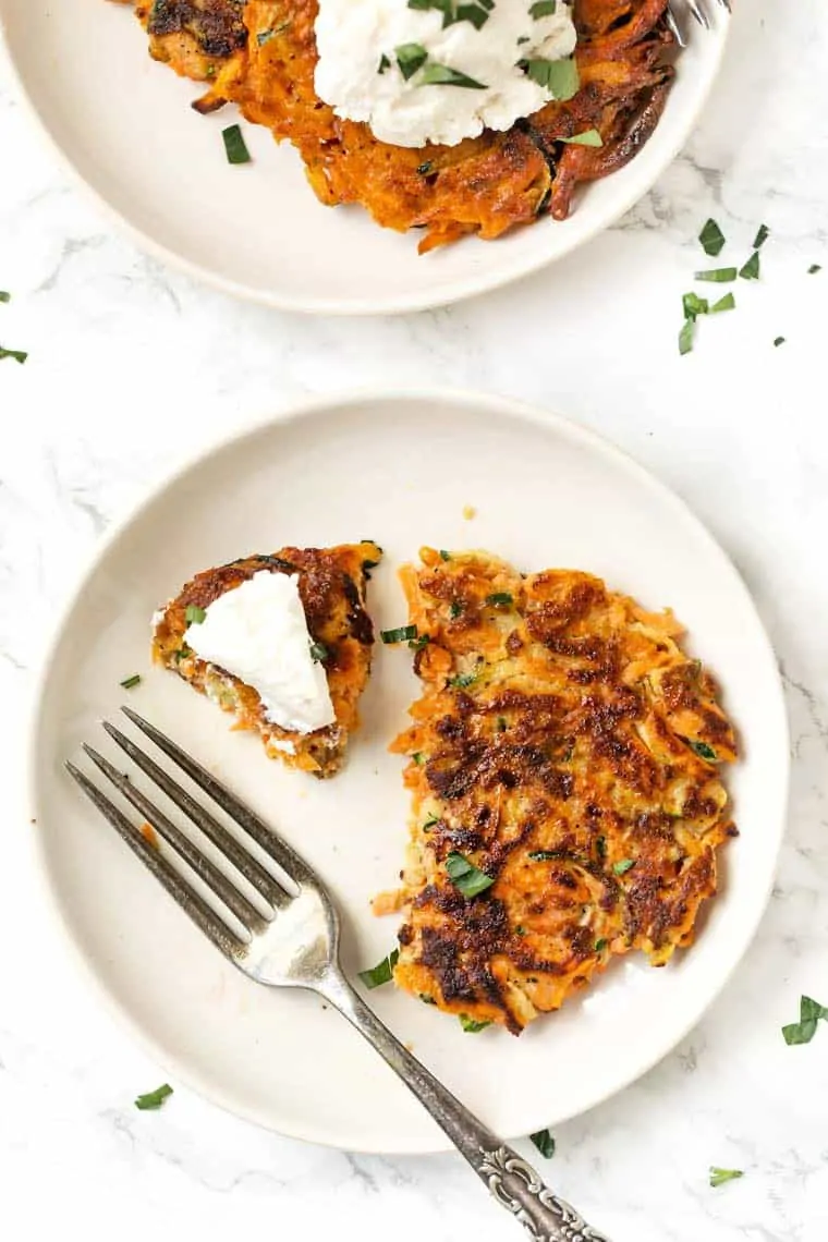 Two plates of veggie fritters topped with cream cheese.