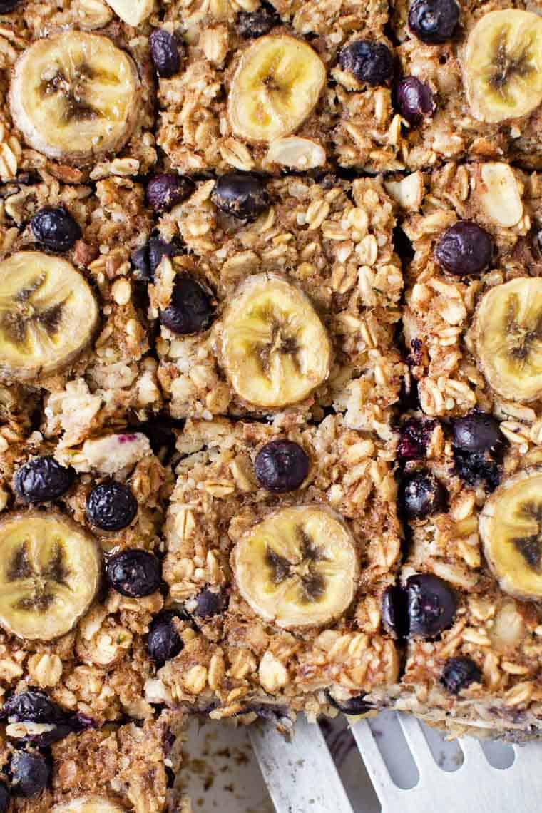 This healthy protein baked oatmeal recipe is gluten-free, vegan and packed with plant protein. Naturally sweetened and full of fresh fruit! Slices of healthy baked oatmeal topped with bananas and blueberries