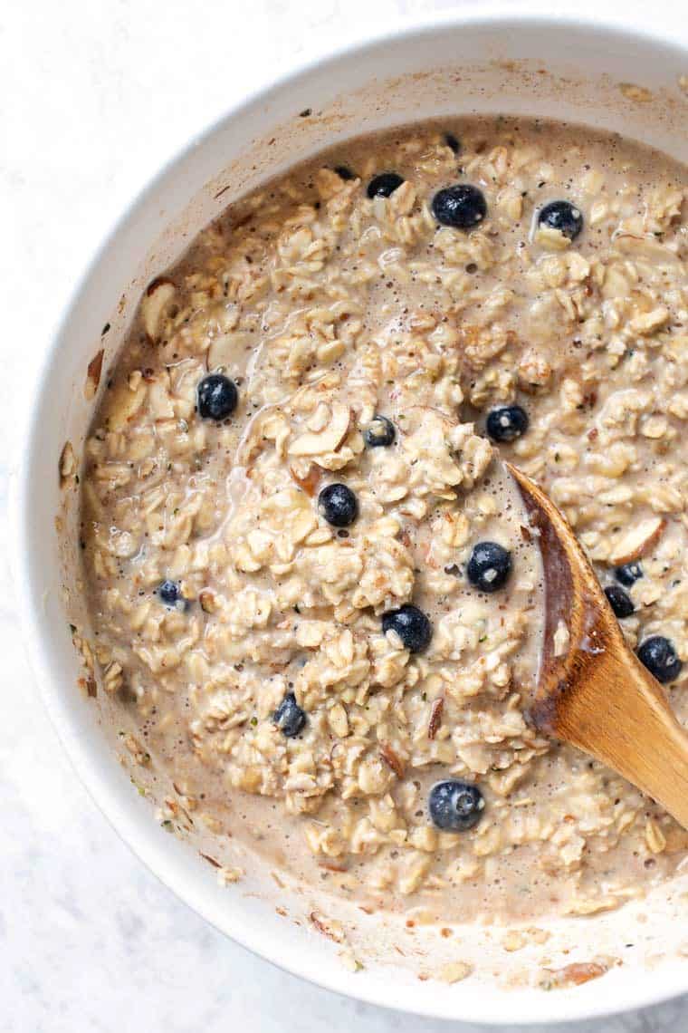 This healthy protein baked oatmeal recipe is gluten-free, vegan and packed with plant protein. Naturally sweetened and full of fresh fruit! Bowl of oats with wooden spoon