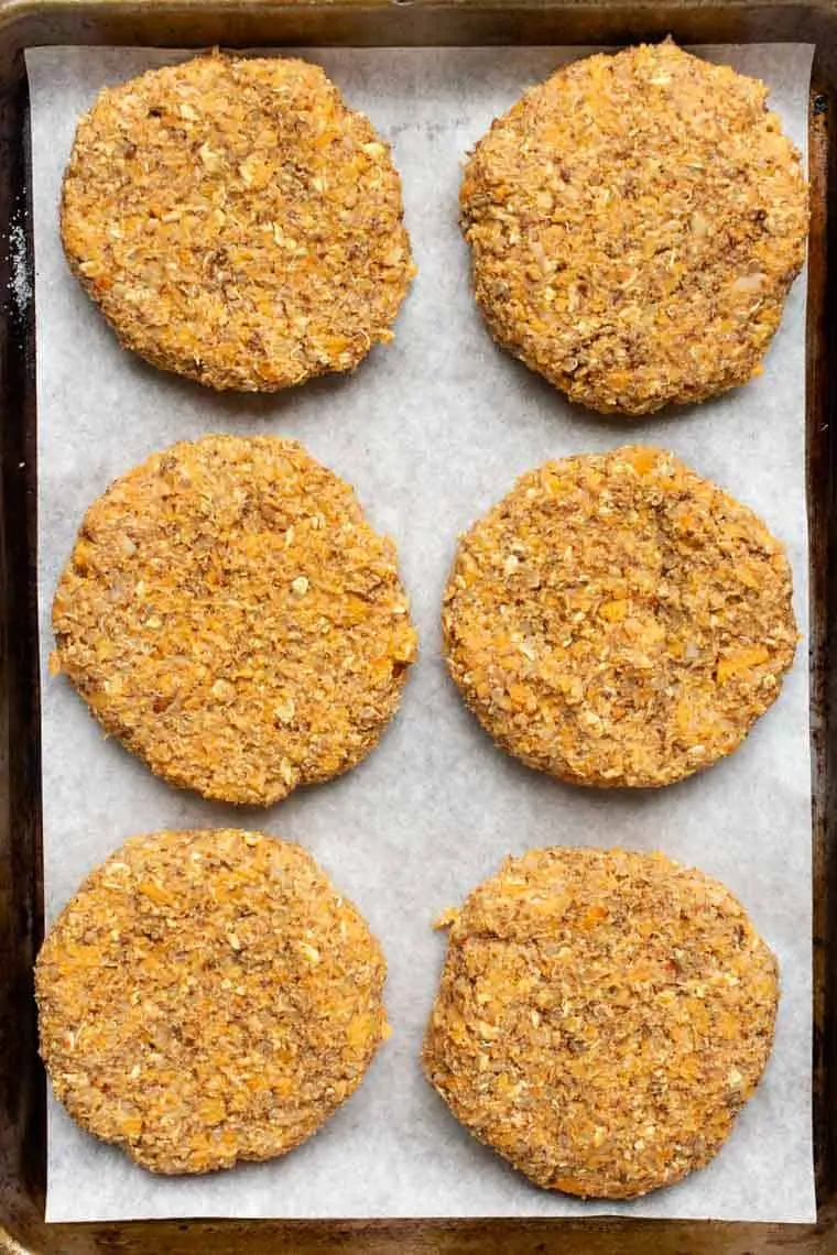 Overhead view of butternut squash white bean burger patties on a parchment-lined baking sheet.