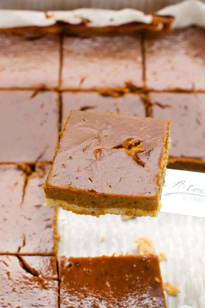 Gluten-, dairy-, and refined sugar-free, these pumpkin pie bars feature a creamy pumpkin pie filling atop a buttery almond flour crust. A spatula lifting a gluten-free pumpkin pie bar from the pan.