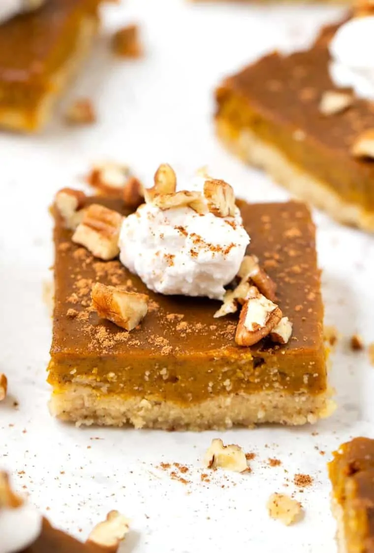 Gluten-, dairy-, and refined sugar-free, these pumpkin pie bars feature a creamy pumpkin pie filling atop a buttery almond flour crust. A gluten-free pumpkin pie bar topped with coconut whipped cream and pecans.