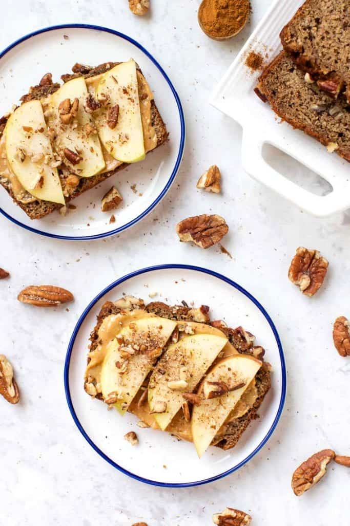 This gluten-free apple banana bread recipe is made with high-protein almond and quinoa flours, apples, and cinnamon for a cozy fall treat! Overhead view of apple banana bread slices topped with peanut butter and apple slices.